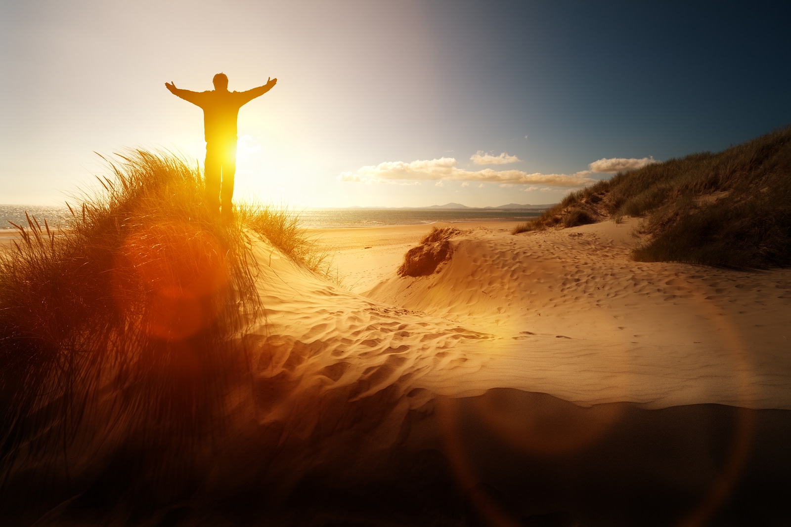 Silhouette of a man with hands raised in the sunset on a beach concept for religion, worship, prayer and praise