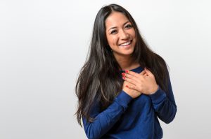 Young woman showing her heartfelt gratitude and thanks clasping her hands to her heart with a pleased smile