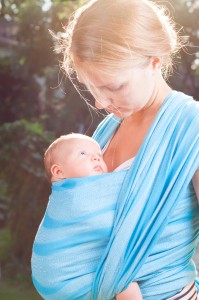 Young mother carrying her little baby girl in blue sling