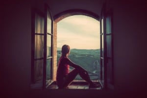 Young woman sitting in an open old window looking on the landsca