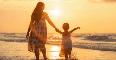 Mãe e filha de mãos dadas andando na praia