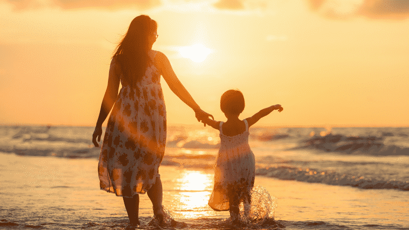 Mãe e filha de mãos dadas andando na praia