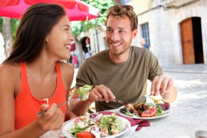 Restaurant tourists couple eating at outdoor cafe. Summer travel people eating healthy food together at lunch during holidays in Mallorca, Spain. Asian Caucasian multiracial young adults.