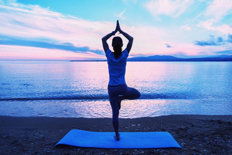Mulher fazendo posição de Yoga em frente ao mar.