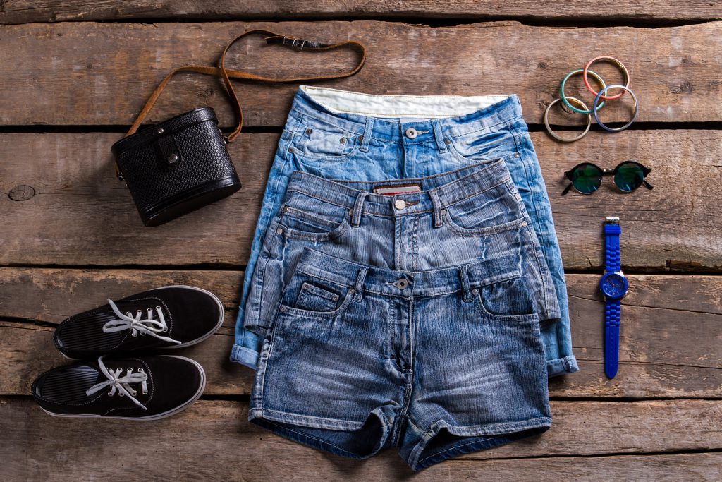 Lady's denim shorts and accessories. Woman's clothing on old floor. Small accessories with denim garments. Simple classic clothes and bracelets.