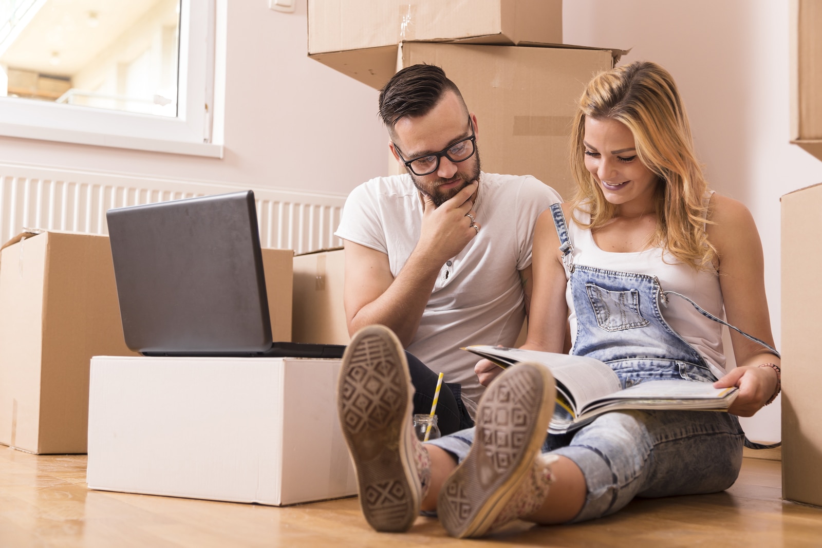 Young couple in love sitting on the floor of their new apartment planning redecoration and searching for ideas on a laptop computer and in a home decorating magazine