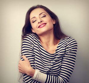 Happy young casual woman hugging herself with natural emotional enjoying face. Love concept by yourself. Vintage closeup portrait