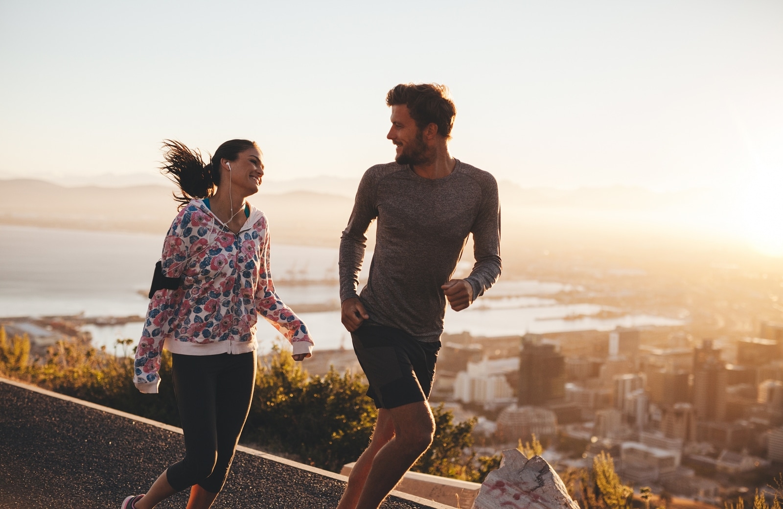 Young couple running together outdoors. Happy young man and woman jogging on country road during sunrise. Two people enjoying morning run.