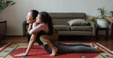 Imagem de uma criança nas costas de sua mãe em um tapete para Yoga