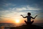 Silhueta de mulher meditando numa praia.