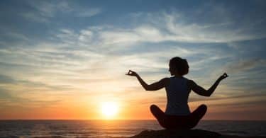 Silhueta de mulher meditando numa praia.