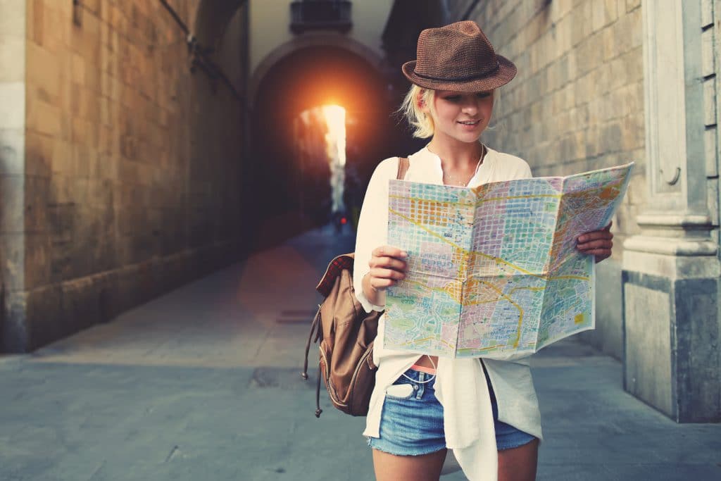 Cheerful woman wanderer with trendy look searching direction on location map while traveling abroad in summer