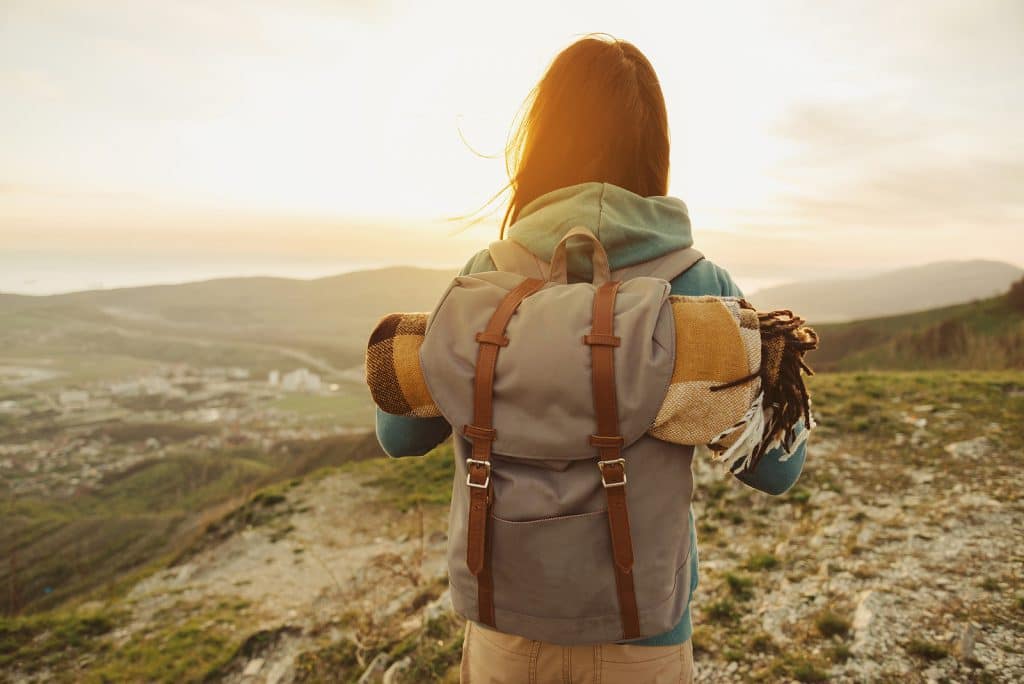 Hiker woman with backpack and sleeping bag walking in the mountains in summer at sunset