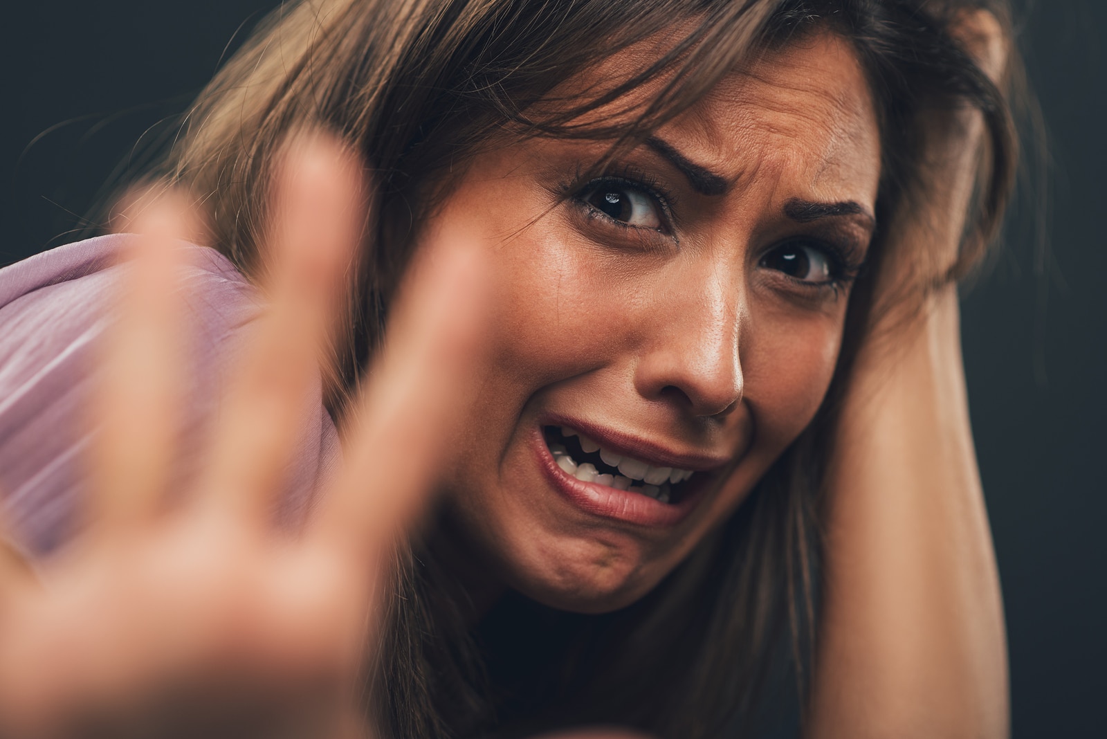 Young abused woman defending with pray looking at camera with outstretched arm. Selective focus. Focus on background on woman face.