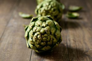 closeup of some raw artichokes on a dark wooden surface
