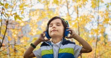 Criança em um parque de olhos fechados segurando seu fone de ouvido