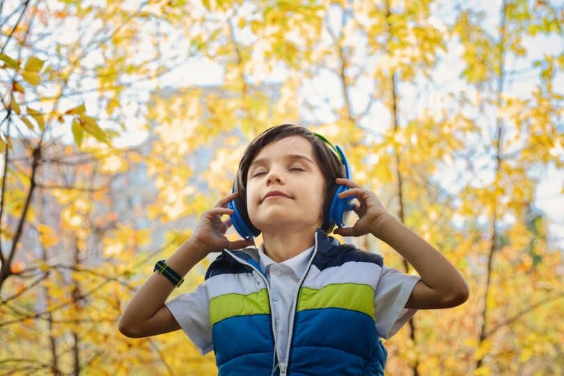 Criança em um parque de olhos fechados segurando seu fone de ouvido