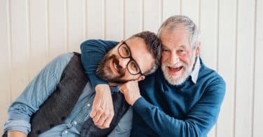 Homens braços abraçados, com expressões sorridentes.