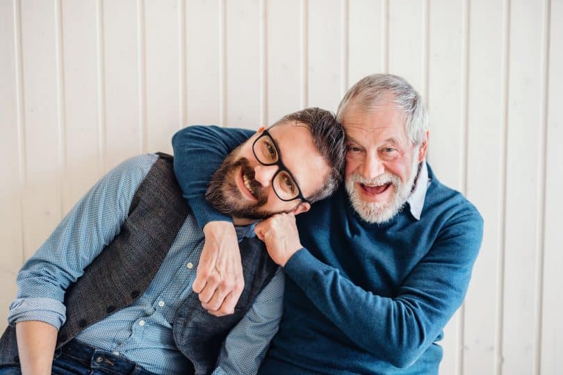 Homens braços abraçados, com expressões sorridentes.