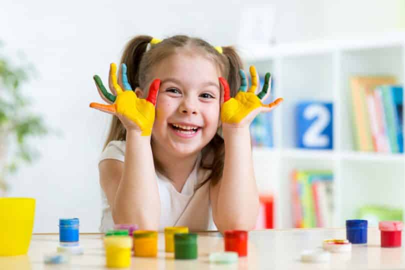 Criança com mãos pintadas de tinta colorida sorrindo