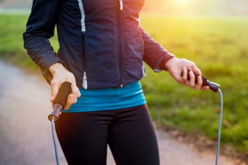 Mulher branca usando roupas esportivas e segurando uma corda de pular nas mãos