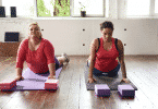 Duas mulheres em uma sala praticando yoga no chão