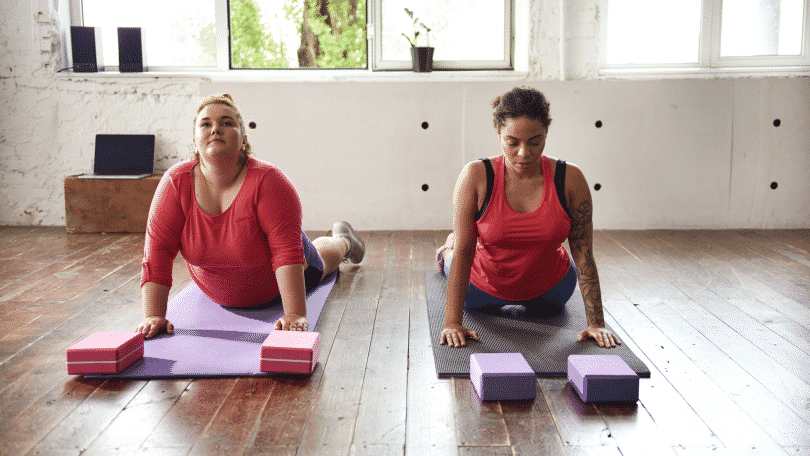 Duas mulheres em uma sala praticando yoga no chão