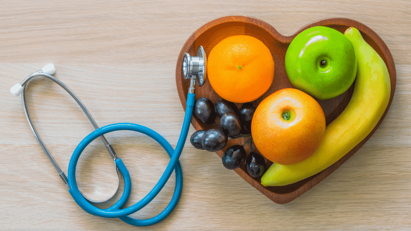 Imagem de frutas em um recipiente em formato de coração. Ao lado, um estetoscópio.