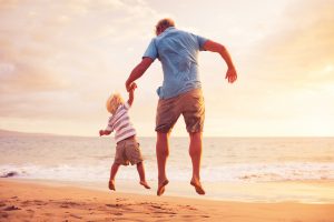 Father and son jumping for joy on the beach at sunset