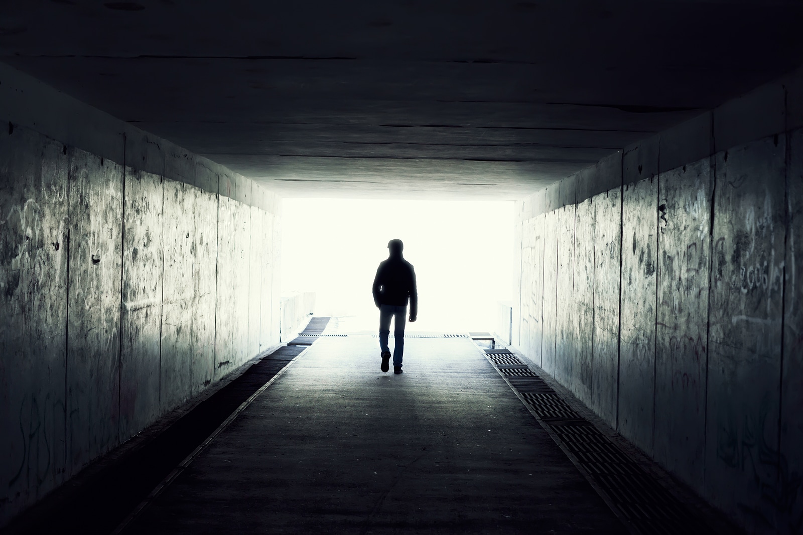 Silhouette Of Man Walking In Tunnel. Light At End Of Tunnel