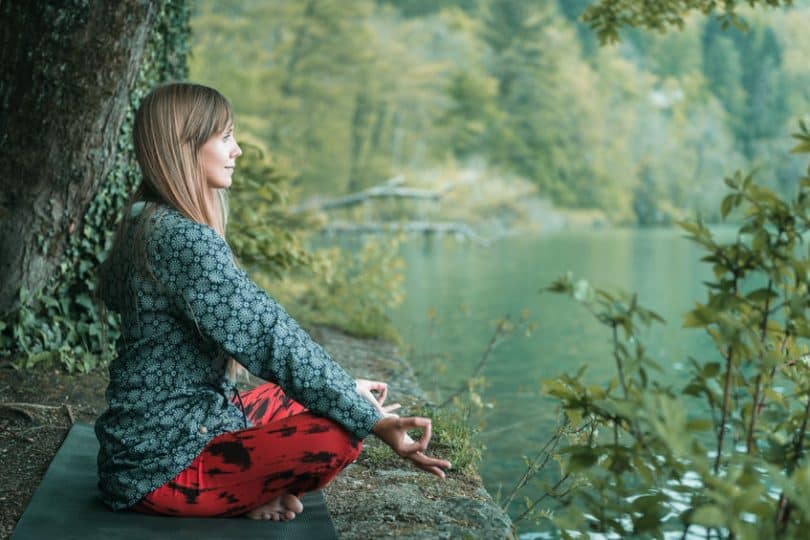 Mulher sentada meditando com lago ao fundo