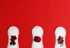 Imagem de três absorventes com a simulação do sangue menstrual em um fundo vermelho