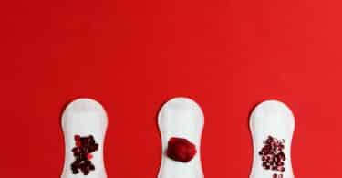 Imagem de três absorventes com a simulação do sangue menstrual em um fundo vermelho