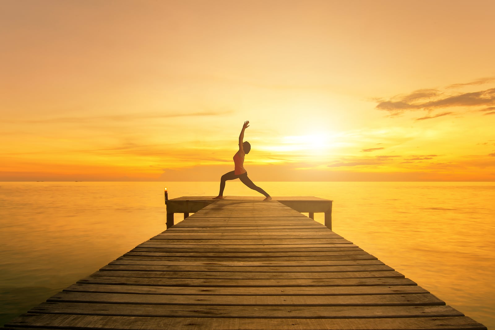 Yoga pose - Woman silhouette practicing yoga Warrior pose on sea bridge at sunset.Yoga near beach.