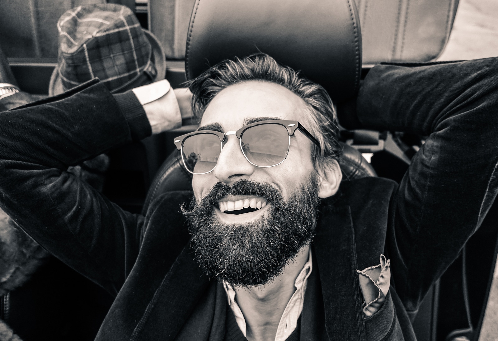 Fashion portrait of young bearded man ready for road trip - Cheerful hipster guy sitting in car lokking the sky - Black and white editing - Soft focus on beard - Warm vintage retro filter