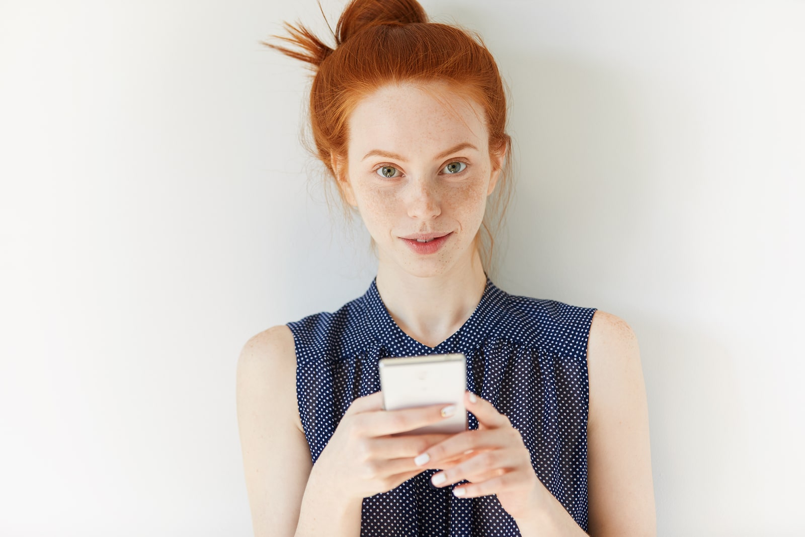 Beautiful young businesswoman in spotted dress reading news or checking email on cell phone. Redhead girl browsing Internet or texting friends using mobile phone. Technology and communication concept