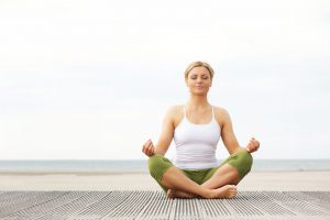 Portrait of a beautiful young woman sitting in yoga pose at the beach