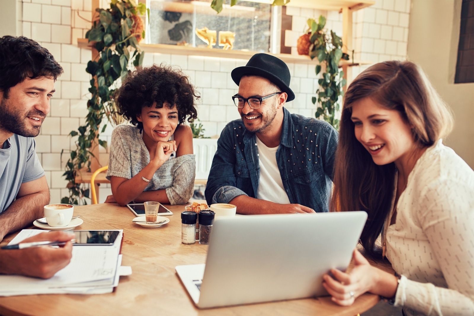 Group of friends hanging out in a coffee shop with a laptop amongst them. Happy young people sitting at restaurant using laptop computer.