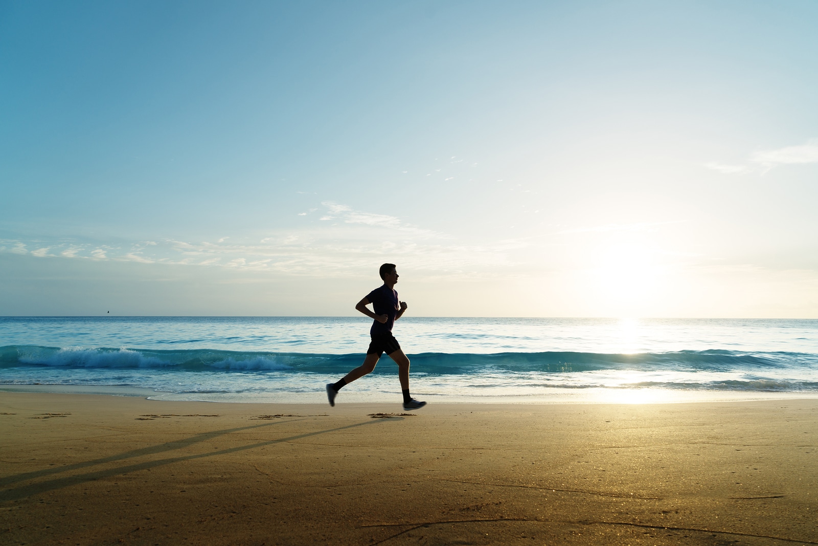 Man running on tropical beach at sunset