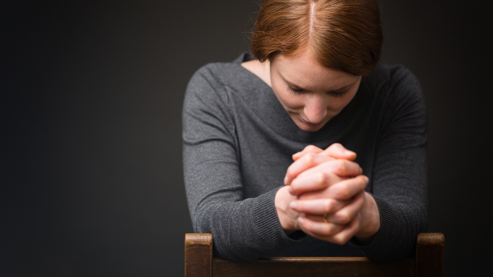 A woman sits on a wooden chair and prays to God.