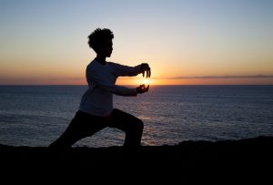young woman performs tai chi moves silhouetted agains sunset