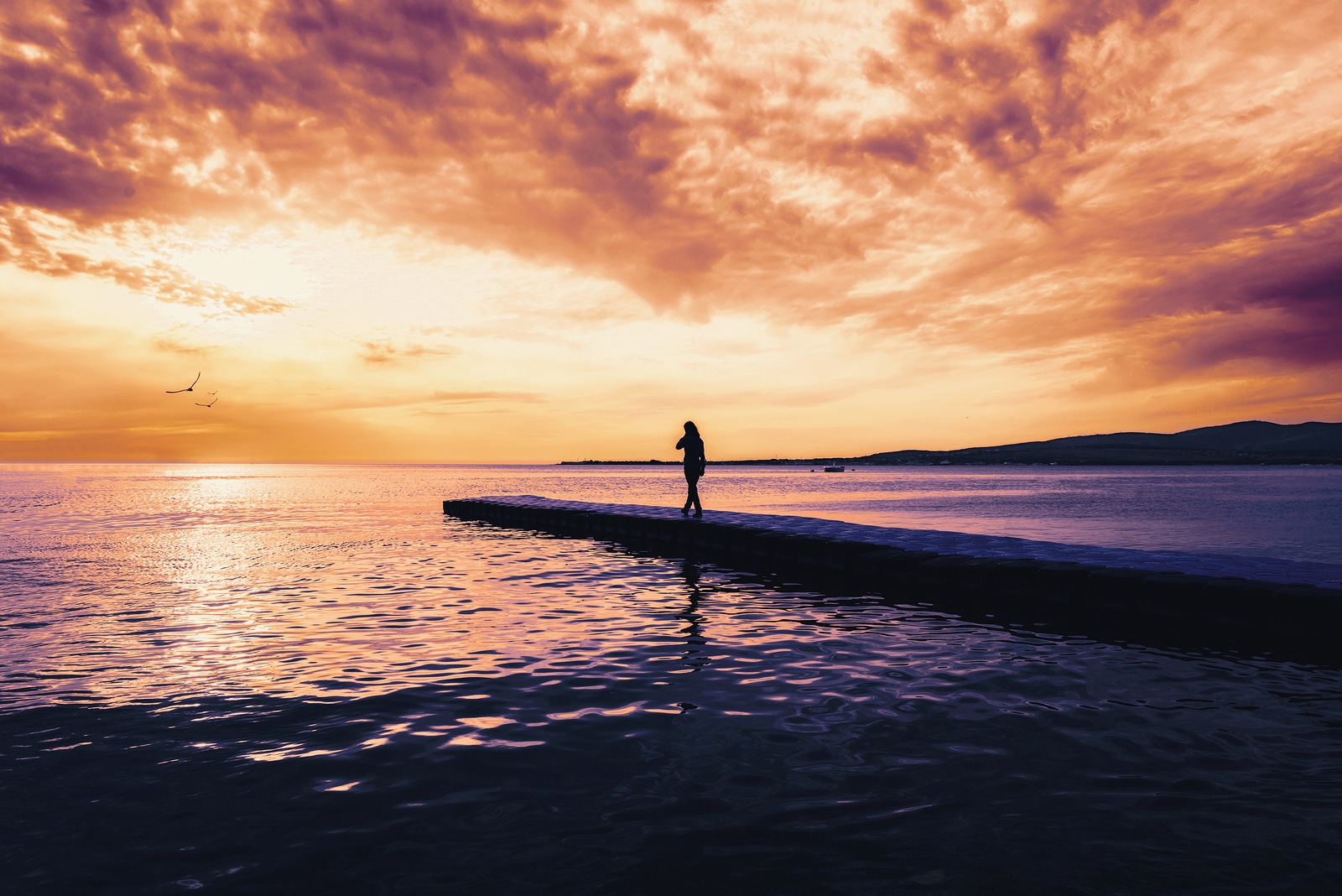 Woman walking on pier near the sea at sunset tranquil scene. Beautiful seascape