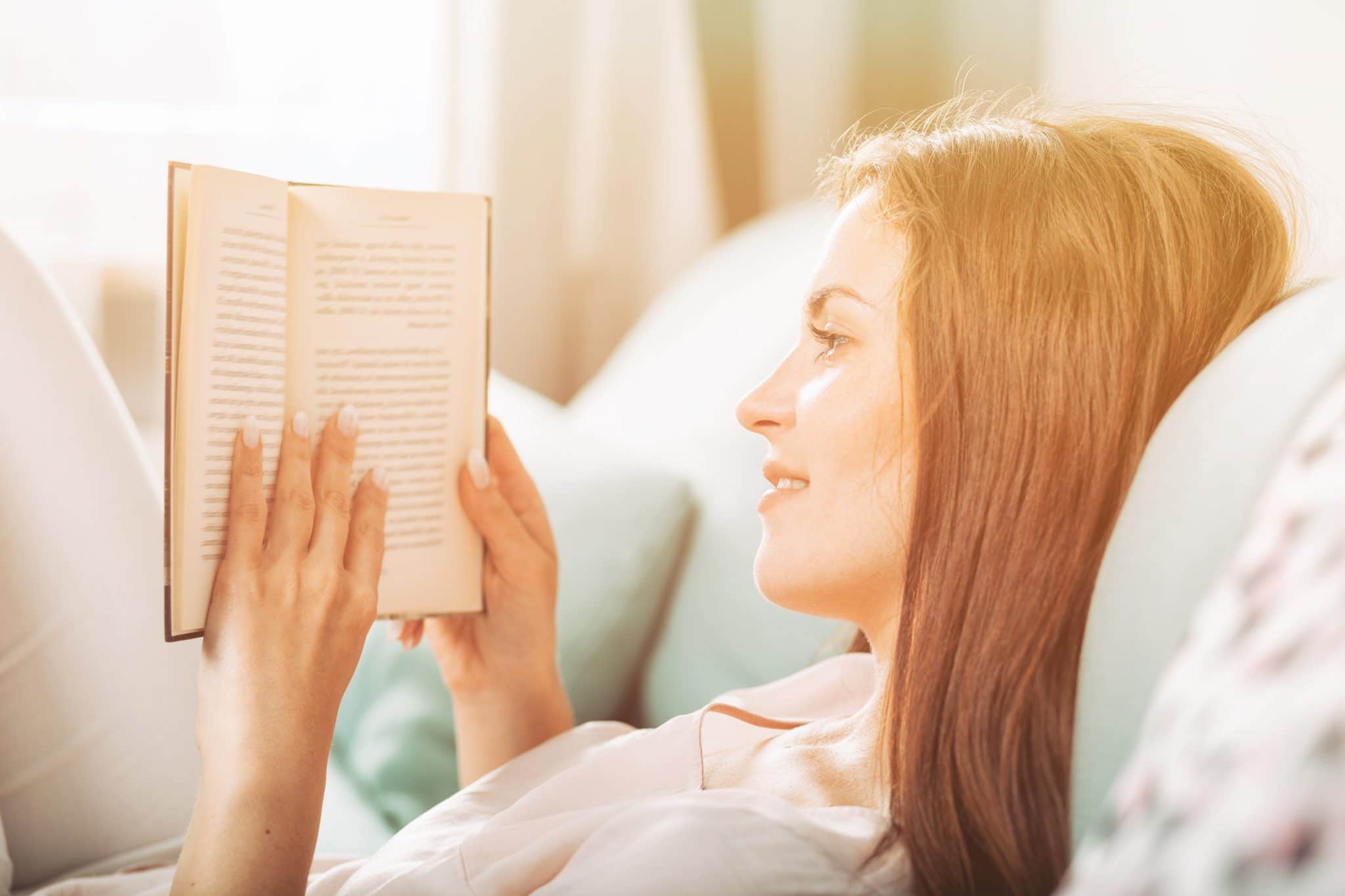 Young woman lying on couch and reading a book at home casual style indoor shoot