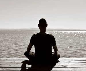 young man seen from behind meditating in the lotus position in an old wooden pier over the sea or over a lake, in black and white