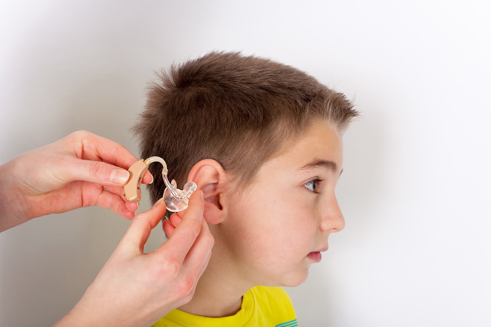 Audiologist putting a hearing aid into young boys ear