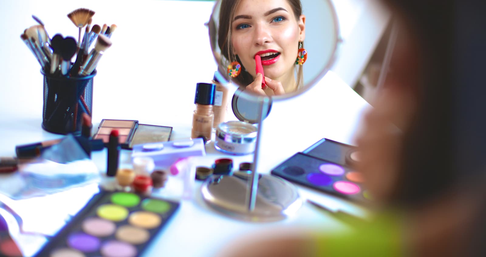 Young beautiful woman making make-up near mirror, sitting at the desk.