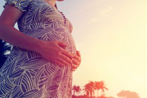 happy pregnant woman on sunset beach touching her belly with love