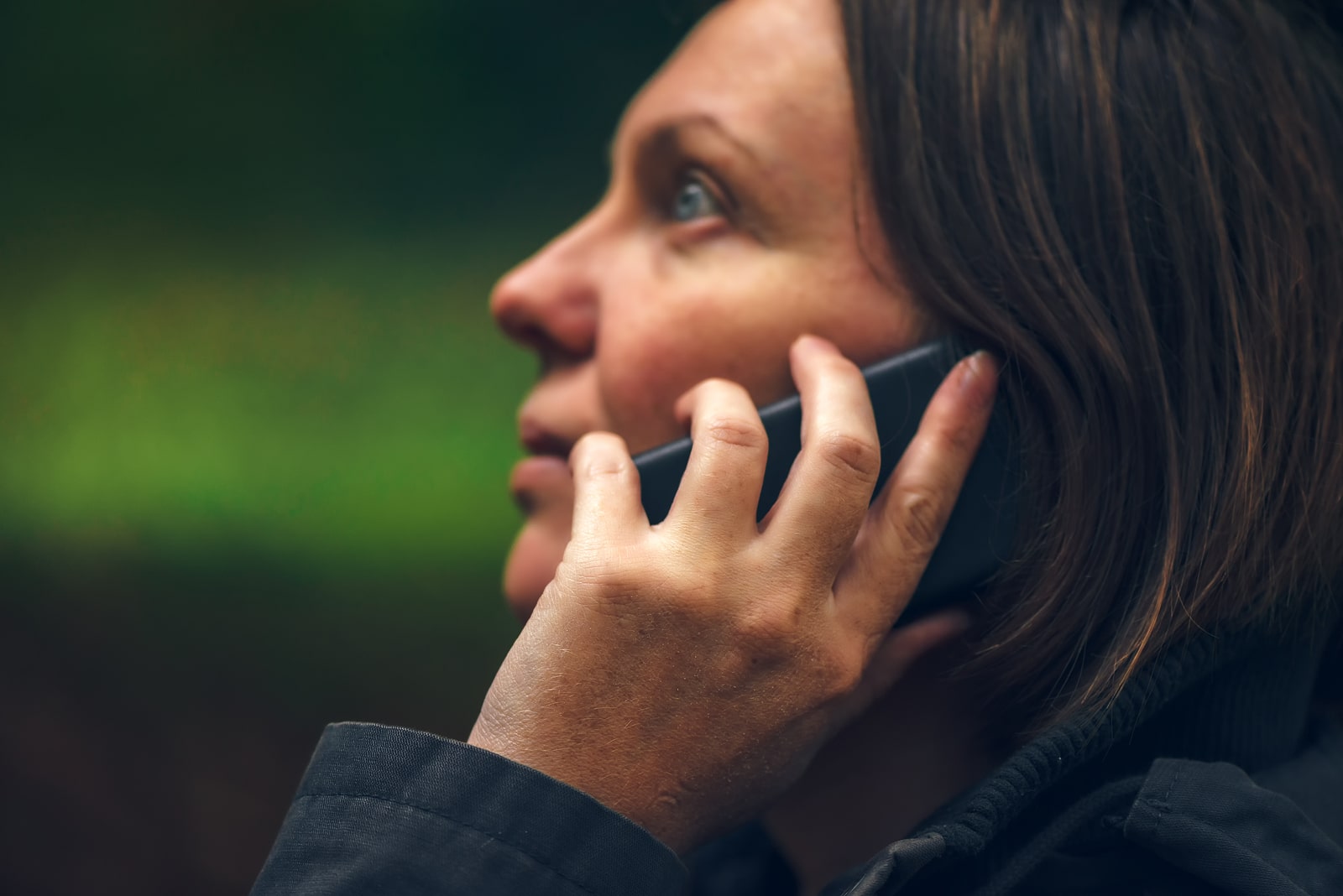 Woman with serious expression talking on mobile phone in park dramatic light coming through treetops and falling on her face