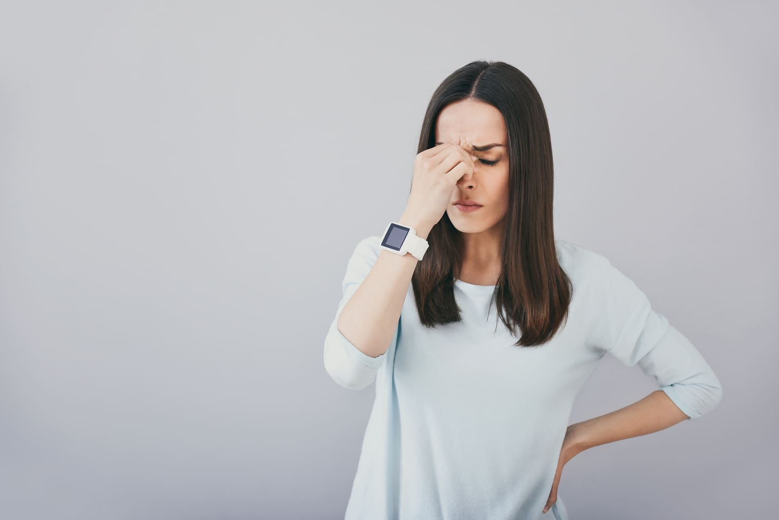 Sad days. Pretty brunette woman touching eyes and feeling tired while standing against white background.