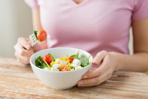 healthy eating, dieting and people concept - close up of young woman eating vegetable salad at home